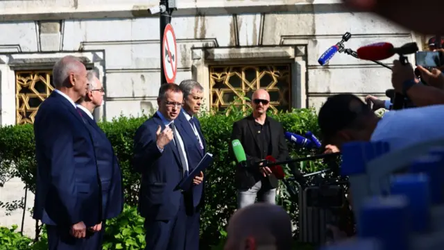 Russian delegations stands in front of members of the press holding out phones and mics as chief negotiator Vladimir Medinsky talks