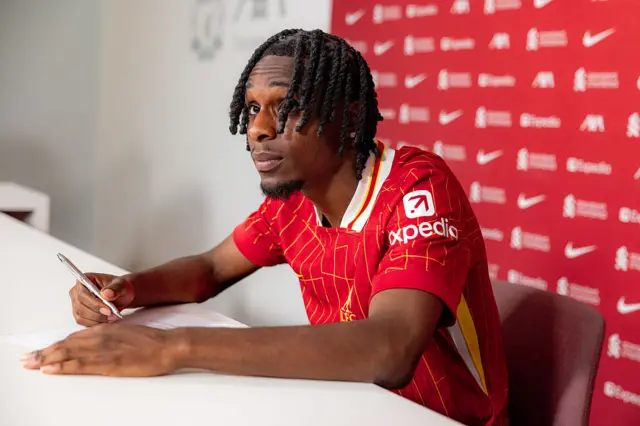 Jeremie Frimpong signing a contract in a Liverpool shirt
