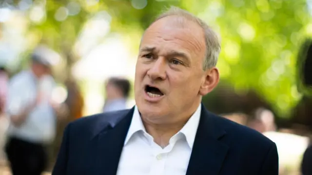A file photo of Ed Davey. He is speaking to someone off camera and wearing a suit without a tie