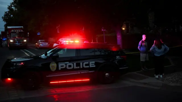 A police car, with a flashing red light, is parked near the scene of the attack in Boulder, Colorado.