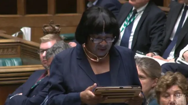 Diane Abbott in black suit and shirt reads from an I-pad in parliament