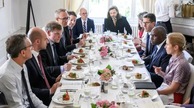 A group of officials sit around a long dining table.