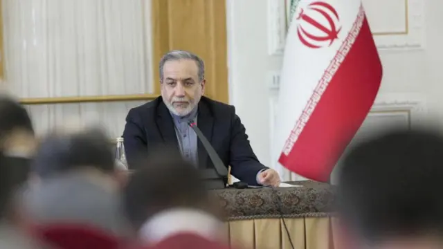 Iran's foreign minister sits behind a microphone at a desk.