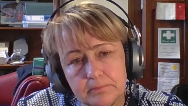Baroness Tanni Grey-Thompson looks at the camera. She has short light brown hair and brown eyes. She is wearing a pair of grey and black headphones.