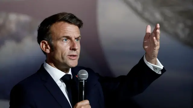 Emmanuel Macron gestures while speaking into a microphone.