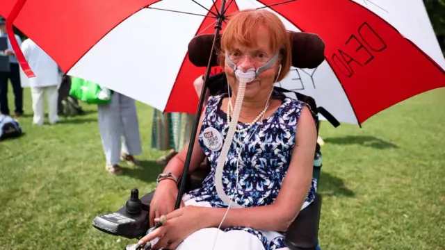 Baroness Campbell under a red and white umbrella