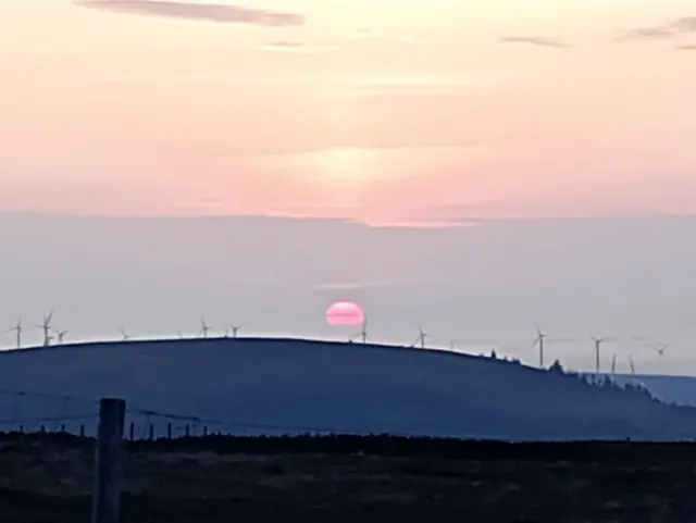 Sun rising over Cairn O'Mount near Banchory. There are a number of wind turbines on the mountain, with the sun peeping through the clouds.