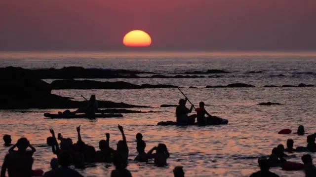 People swim in the sea and watch as the sun rises on the horizon