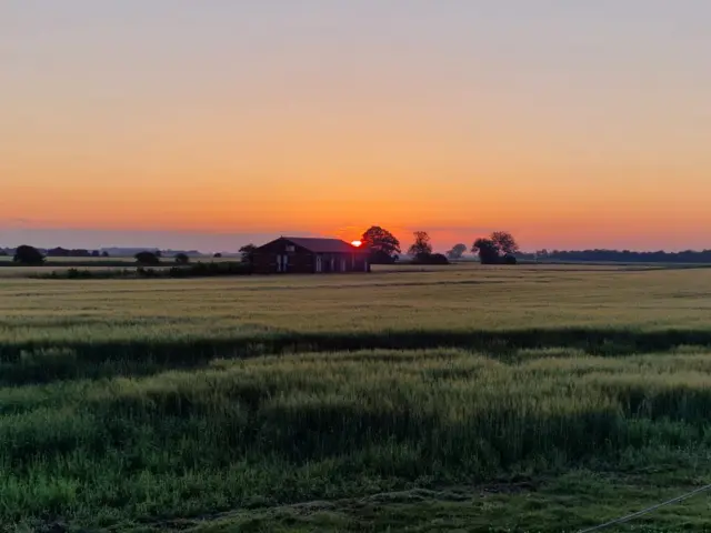 The sun rising over a rural building and a field in Spalding. There is large field to the centre of the image.