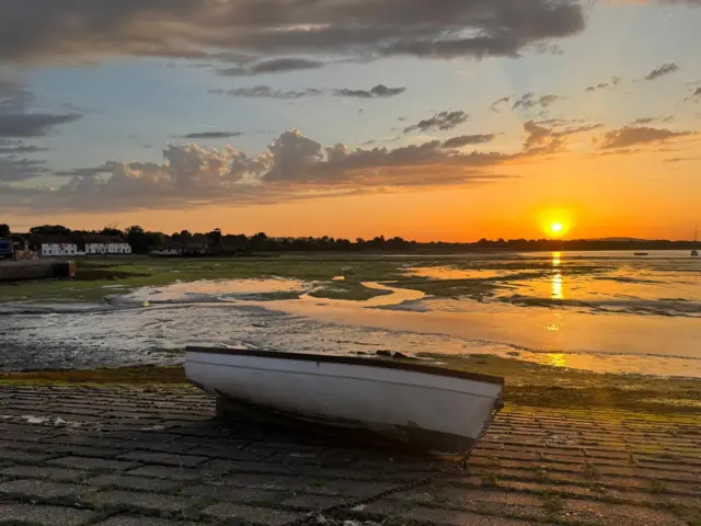 The run rising over an empty harbour. There is a singular boat to the centre of the image.