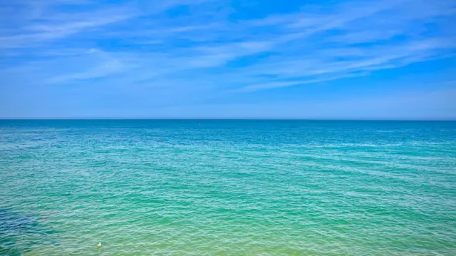 Green and blue seawater underneath a clear blue sky