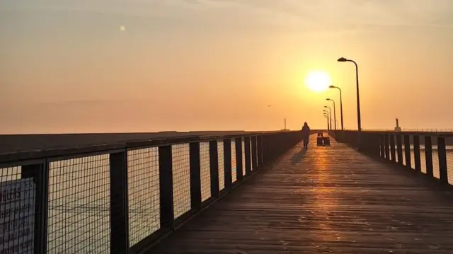 A person walking on a wooden pier in Northumberland.