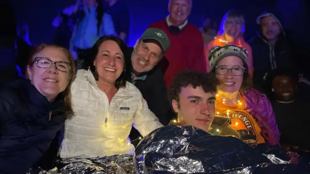 Five people looking into camera. Three women and one man. It's dark, the people are smiling.