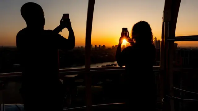 A couple take photos on mobile phones of the sun rising from a pod on the London Eye.