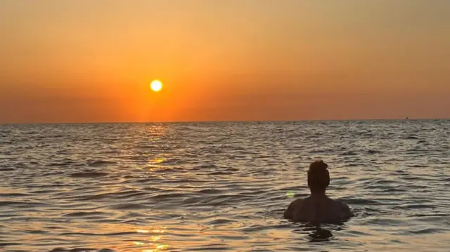 A woman swimming in the sea, looking out at the sunrise.