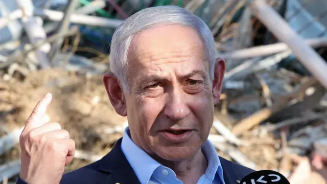 Netanyahu speaks wearing a suit in front of destroyed building.