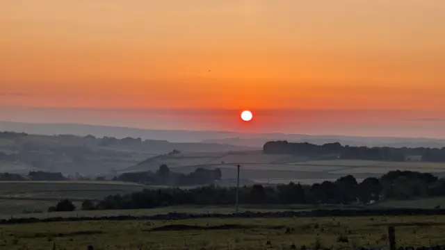 The sunrise over the fields in Derbyshire. The sun is central to the image, with the fields separated by hedgerows.