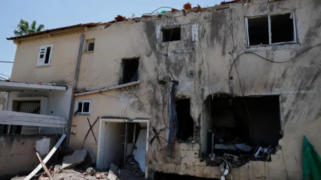 A damaged building, with windows shattered and a big hole in the wall.