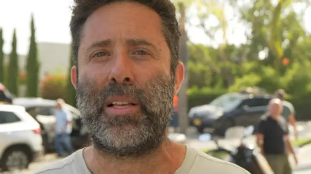 Eran Levi looks at the camera. He has a brown beard and brown hair and blue eyes, He is wearing a grey t-shirt.