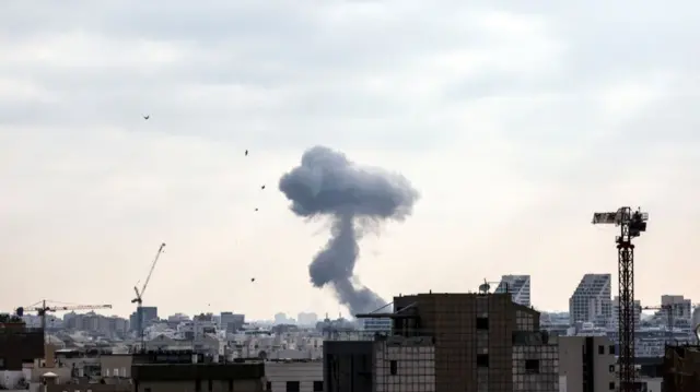 White smoke billows over a residential area of Tel Aviv, cranes and tall buildings in the foreground