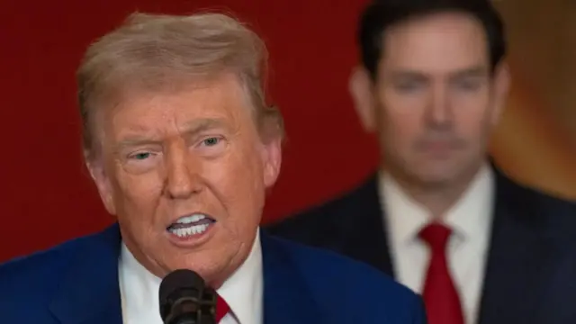 Trump speaks behind a microphone, Rubio stands in the background.