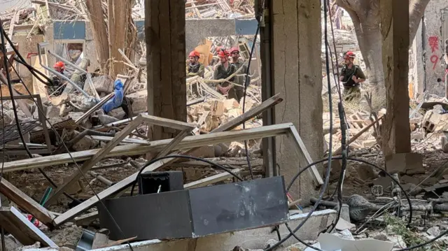 Several rescue workers look on at the damage caused by an Iranian missile attack.