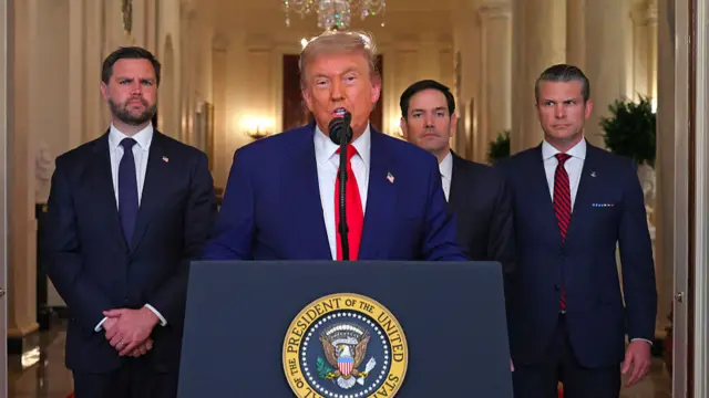 Trump stands behind a podium and speaks, flanked by Vance, Rubio and Hegseth. They all wear suits.