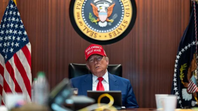 Donald Trump sits in the situation room and wears a red MAGA hat.