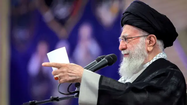 A side view of Ayatollah Ali Khamenei, pointing, as he speaks into a microphone