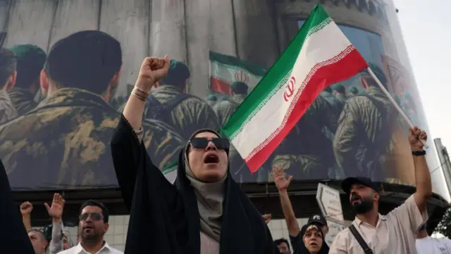 A woman stands at a demonstration in Tehran, Iran. A man waves an Iranian flag behind her