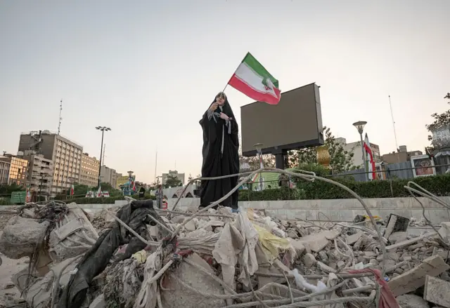 An Iranian art student waves a country flag by a destroyed building in Tehran on Saturday