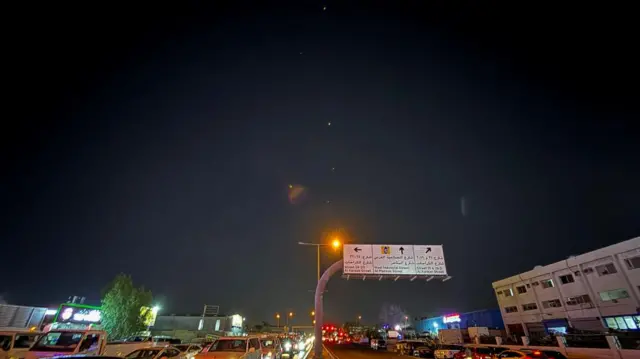 Small white lights can be seen in the sky above a road in Qatar on which cars are travelling