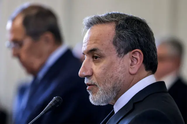 Side profile of Iran's Foreign Minister Abbas Araghchi, wearing a dark suit and in front of a microphone