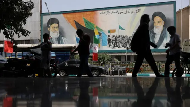 People walk next to a mural with a picture of Iran's Supreme Leader on a street