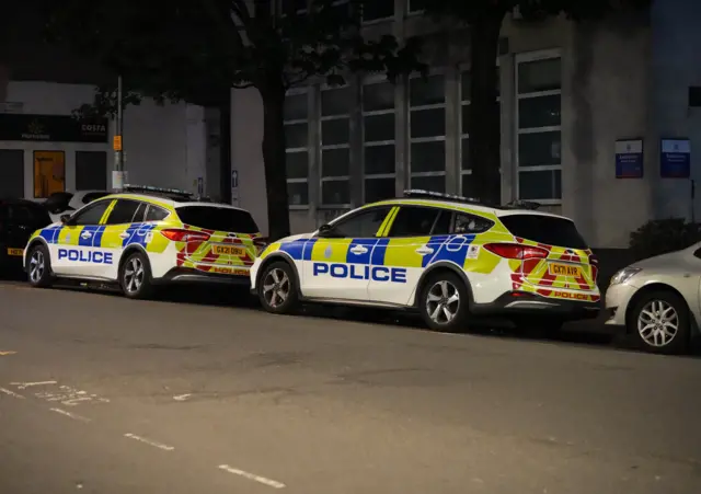 Two police cars parked by the side of a road at night.