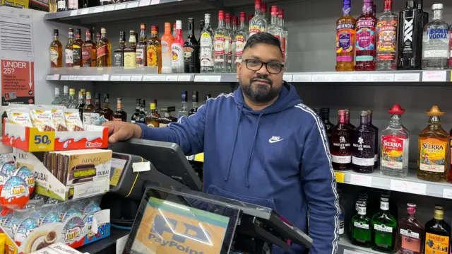 A man stands behind a shop counter.