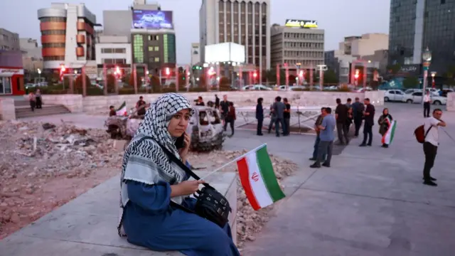 A woman holds an Iranian flag while sitting on a bench in Tehran.