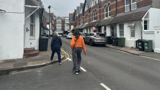 Residents walking away from camera walking down a street in Eastbourne returning to their homes