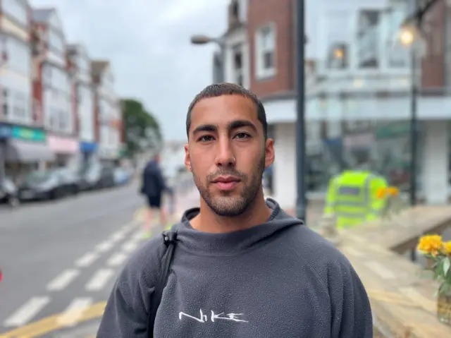 A man in a grey jumper and short cropped hair.