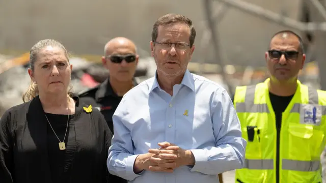 Israel's president Isaac Herzog stands next to other people at the site of an Iranian missile attack.