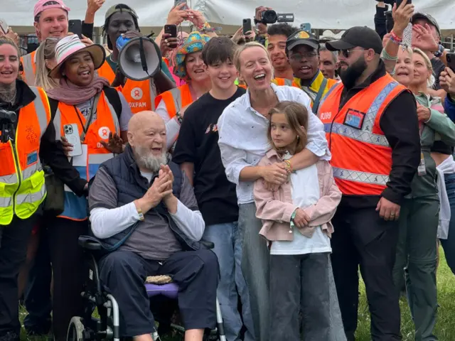 Emily and Michael Eavis stand with their family as the gates are flung open. They are smiling and cheering