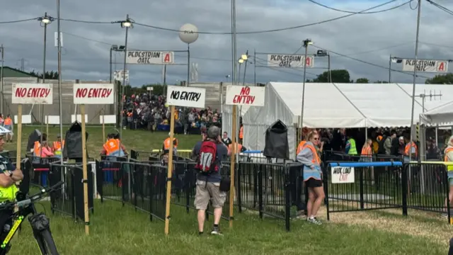 Pedestrian Gate A at Glastonbury Festival. People can been seen walking through and queuing at the gate