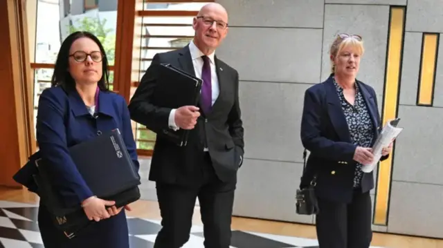 First Minister John Swinney walks towards the Holyrood chamber flanked by Deputy First Minister Kate Forbes and Finance Secretary Shona Robison