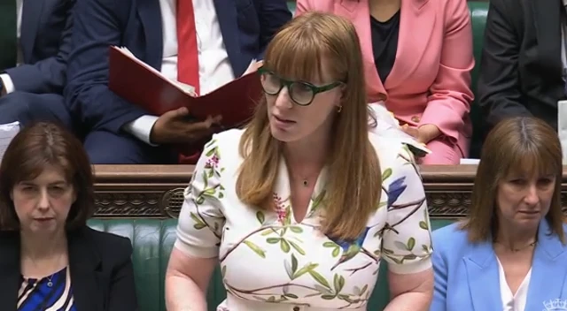 A picture of Angela Rayner in floral dress answering questions in the House of Commons. To her left, in a blue blazer is Chancellor Rachel Reeves