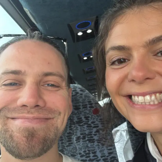 Charlie and Hattie smiling into camera, sat on a coach.