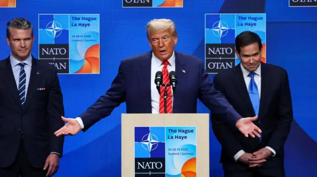 Trump stands at a podium, with his arms outstretched, while Rubio stands behind him, a smile on his face, with Hegseth also smiling