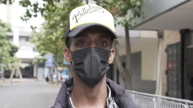 A man wearing a baseball cap and a black face mask