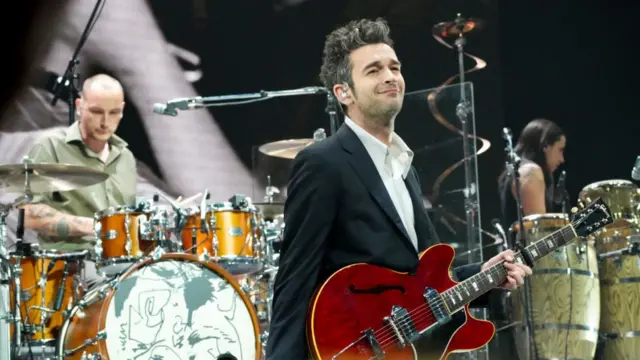 The 1975 lead singer Matty Healy on stage in a black blazer and white shirt with a Red Gibson 330. Other