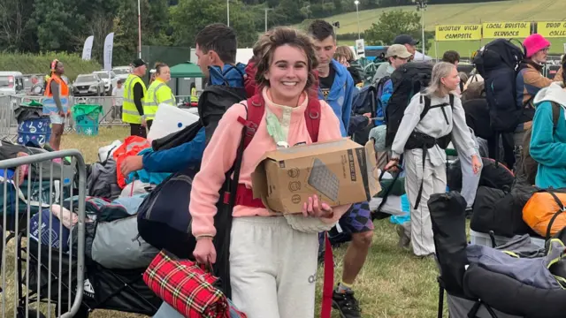 A woman with a pink jumper on holding her bags as she walks into Glastonbury Festival