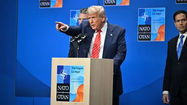 Donald Trump points while taking questions at a Nato summit podium